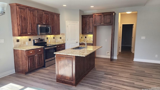 kitchen featuring sink, wood-type flooring, an island with sink, stainless steel appliances, and light stone countertops