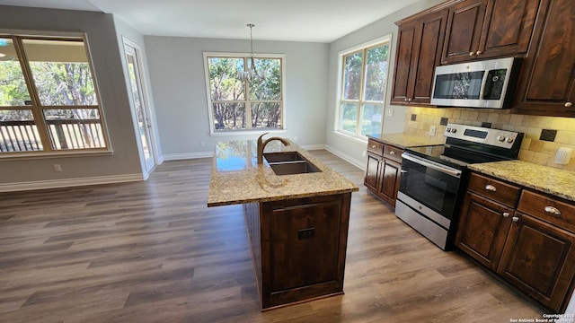 kitchen with pendant lighting, sink, appliances with stainless steel finishes, a kitchen island with sink, and light stone countertops