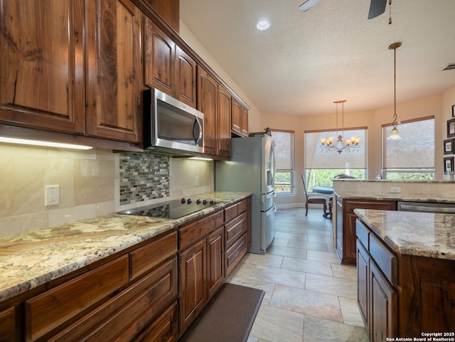 kitchen with pendant lighting, ceiling fan with notable chandelier, light stone countertops, tasteful backsplash, and stainless steel appliances