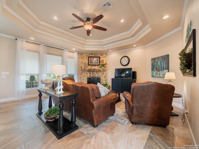 living room featuring crown molding, ceiling fan, a fireplace, visible vents, and a raised ceiling