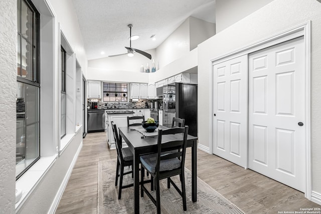 dining area featuring vaulted ceiling, ceiling fan, light hardwood / wood-style floors, and a textured ceiling