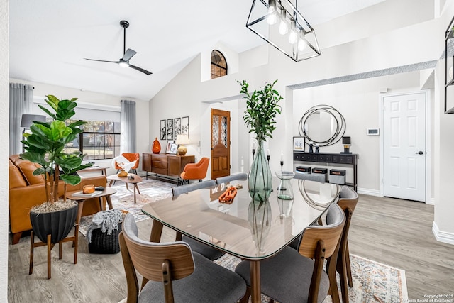 dining space featuring high vaulted ceiling, ceiling fan with notable chandelier, and light wood-type flooring