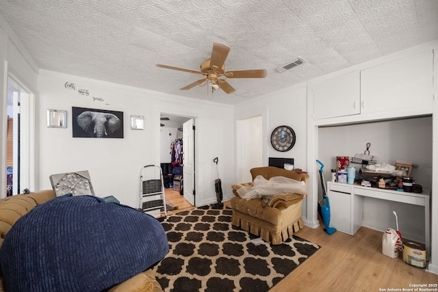 bedroom with a textured ceiling, a walk in closet, ceiling fan, and light wood-type flooring