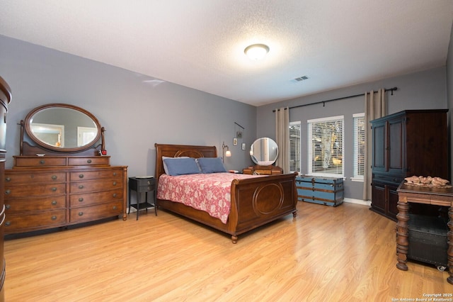 bedroom with visible vents, a textured ceiling, and light wood finished floors