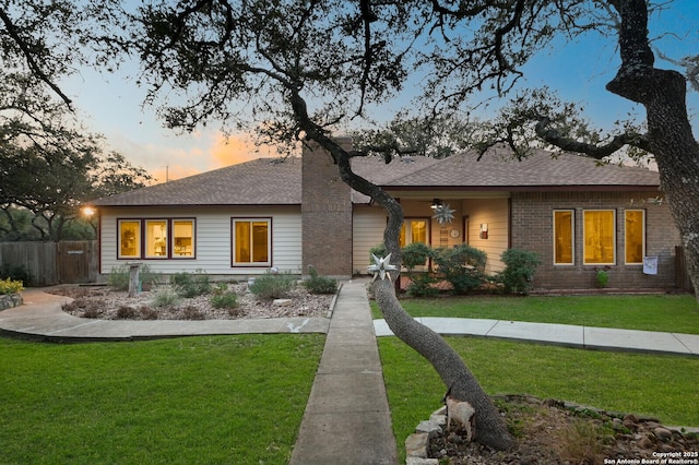 exterior space with roof with shingles, brick siding, a yard, and fence