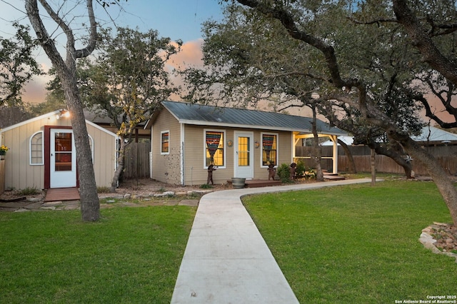 view of front of property featuring a yard, an outbuilding, metal roof, and fence