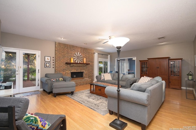 living room with french doors, visible vents, light wood-style flooring, a brick fireplace, and baseboards