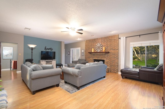 living area featuring baseboards, a ceiling fan, light wood-style flooring, a textured ceiling, and a brick fireplace