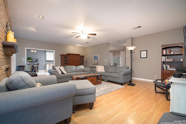 living area with light wood-style flooring, a fireplace, visible vents, a ceiling fan, and baseboards