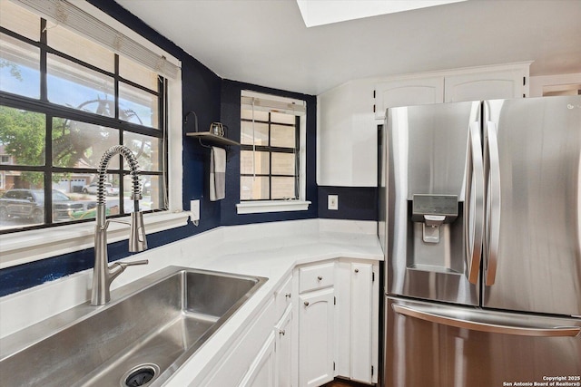 kitchen with white cabinets, sink, stainless steel fridge, and a skylight