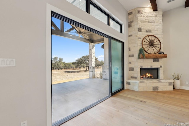 entryway featuring light hardwood / wood-style flooring, ceiling fan, an outdoor stone fireplace, a high ceiling, and beamed ceiling