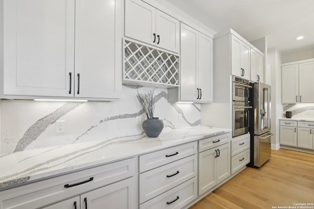 kitchen with decorative backsplash, light hardwood / wood-style flooring, stainless steel appliances, and white cabinets