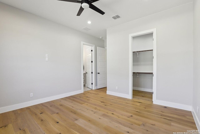 unfurnished bedroom with a walk in closet, a closet, ceiling fan, and light wood-type flooring