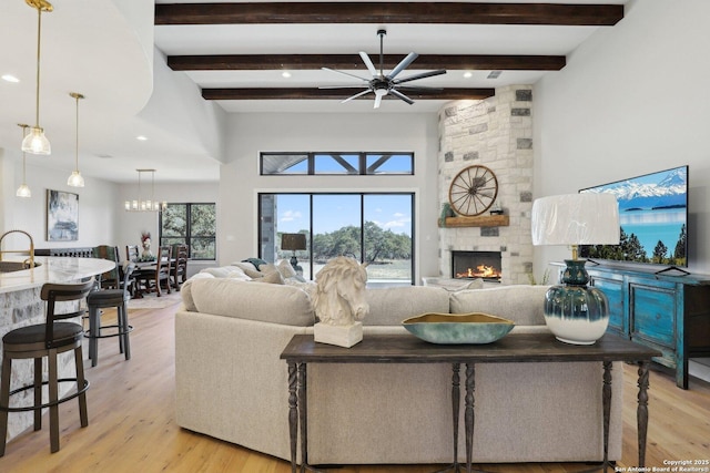 living room with sink, ceiling fan, a stone fireplace, beamed ceiling, and light wood-type flooring