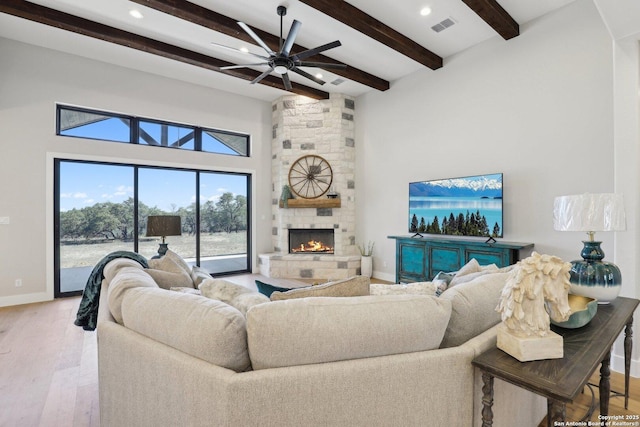 living room featuring hardwood / wood-style flooring, ceiling fan, beam ceiling, a towering ceiling, and a stone fireplace