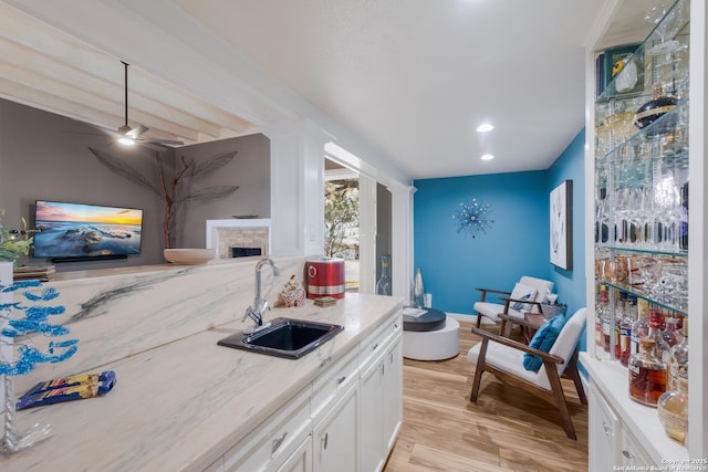 kitchen with sink, white cabinetry, ceiling fan, light stone countertops, and light hardwood / wood-style floors