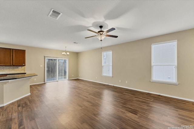 unfurnished living room featuring ceiling fan with notable chandelier and dark hardwood / wood-style floors