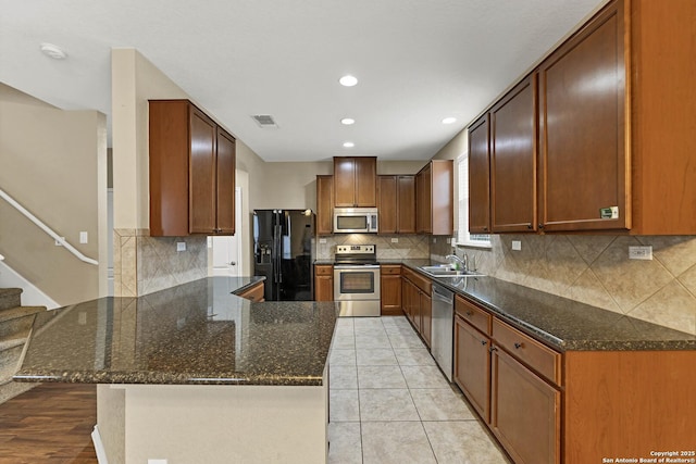 kitchen featuring sink, stainless steel appliances, light tile patterned flooring, kitchen peninsula, and dark stone counters