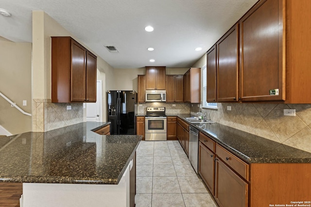 kitchen featuring sink, light tile patterned floors, dark stone countertops, stainless steel appliances, and kitchen peninsula