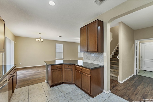 kitchen featuring decorative light fixtures, light tile patterned floors, stainless steel dishwasher, kitchen peninsula, and backsplash