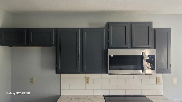 kitchen featuring a textured ceiling, marble finish floor, dark cabinetry, light stone countertops, and stainless steel microwave