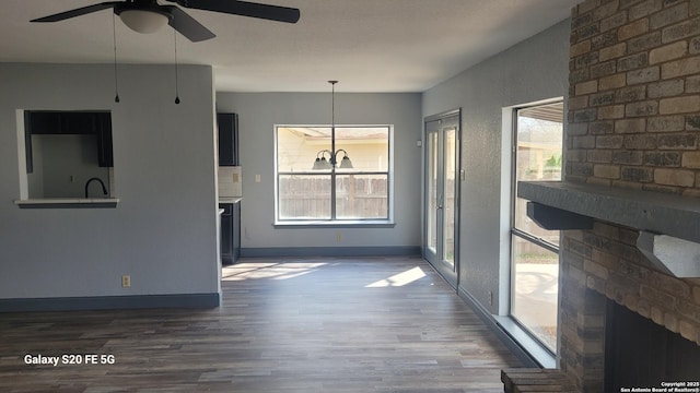 unfurnished living room featuring plenty of natural light, dark wood-type flooring, and a brick fireplace