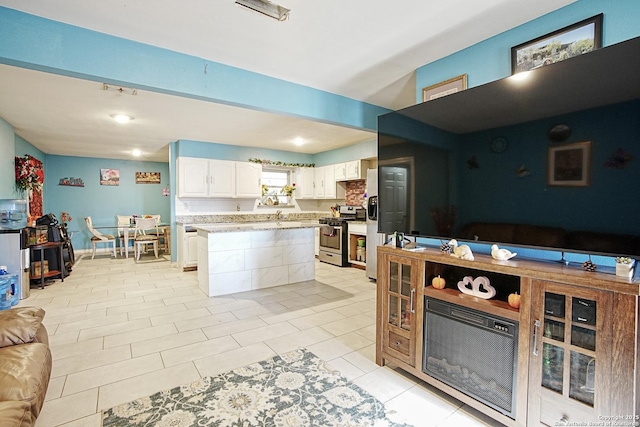 kitchen with light tile patterned floors, stainless steel gas range, a breakfast bar, a center island, and white cabinets