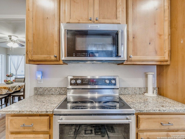 kitchen with light stone countertops, stainless steel appliances, and ceiling fan