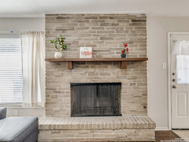 room details with wood-type flooring, a brick fireplace, ornamental molding, and a textured ceiling