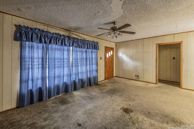 spare room featuring light colored carpet, a textured ceiling, ornamental molding, wooden walls, and ceiling fan