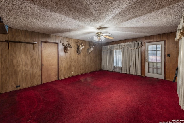 unfurnished room featuring carpet, a textured ceiling, ceiling fan, and wood walls