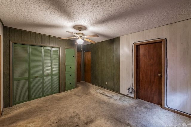 unfurnished bedroom featuring ceiling fan, carpet, a textured ceiling, a closet, and wood walls