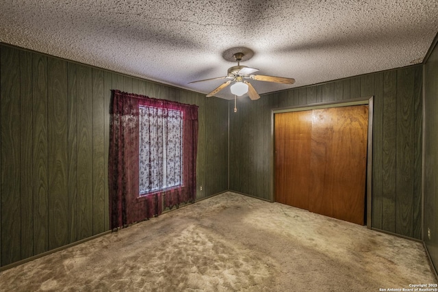 unfurnished bedroom with a textured ceiling, wooden walls, a closet, ceiling fan, and carpet