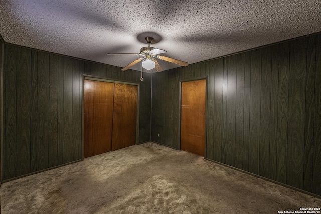 unfurnished bedroom with ceiling fan, wooden walls, carpet, a textured ceiling, and a closet