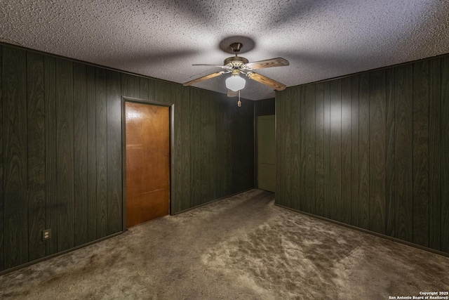 carpeted spare room with ceiling fan, wooden walls, and a textured ceiling