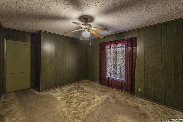 empty room with ceiling fan, carpet floors, a textured ceiling, and wood walls