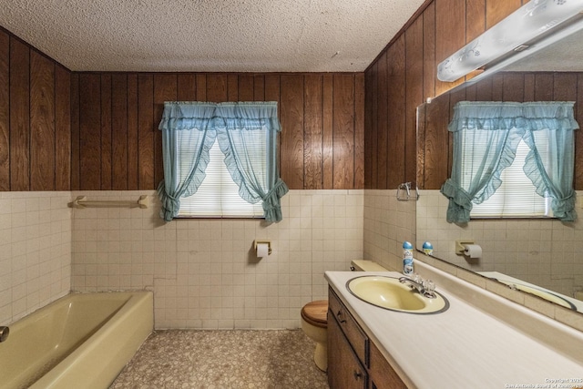 bathroom featuring toilet, a textured ceiling, vanity, wooden walls, and a tub