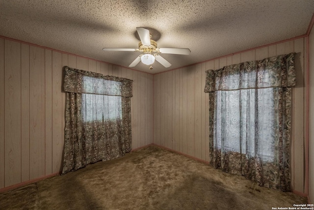 carpeted spare room with a textured ceiling, ornamental molding, ceiling fan, and wood walls