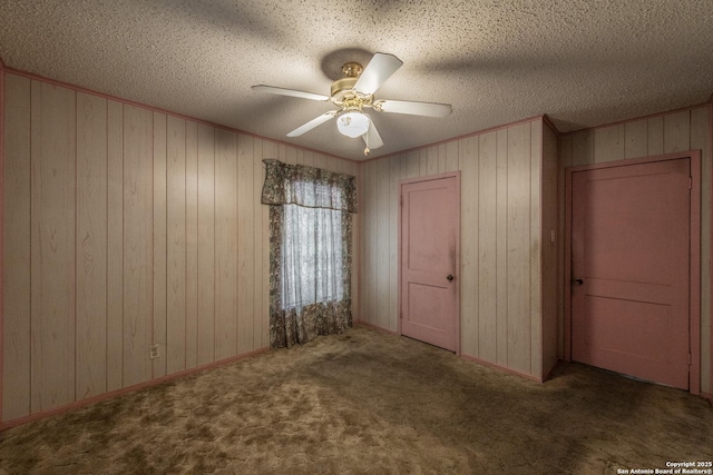 carpeted empty room featuring crown molding, a textured ceiling, ceiling fan, and wood walls