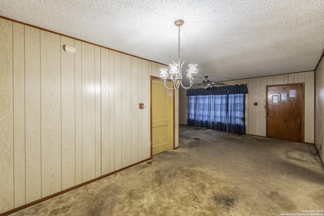 unfurnished dining area with a notable chandelier, wood walls, a textured ceiling, and dark colored carpet