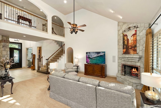 living room with ceiling fan, high vaulted ceiling, a stone fireplace, and carpet floors