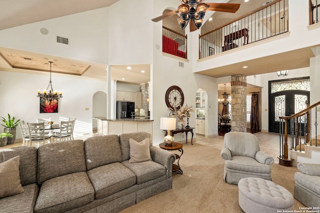 living room with light carpet, ceiling fan with notable chandelier, ornamental molding, and a high ceiling