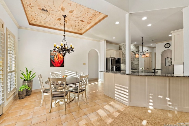 kitchen featuring an inviting chandelier, stainless steel fridge, a raised ceiling, pendant lighting, and dark stone counters