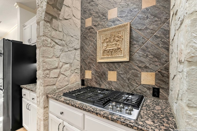 kitchen with crown molding, appliances with stainless steel finishes, white cabinetry, tasteful backsplash, and dark stone counters