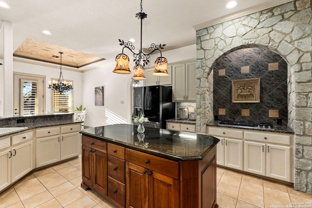 kitchen with decorative light fixtures, a tray ceiling, dark stone counters, decorative backsplash, and black appliances