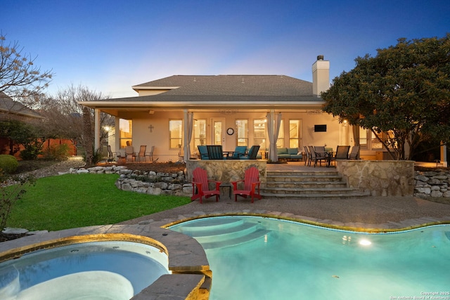 pool at dusk featuring a lawn, a patio, and an in ground hot tub