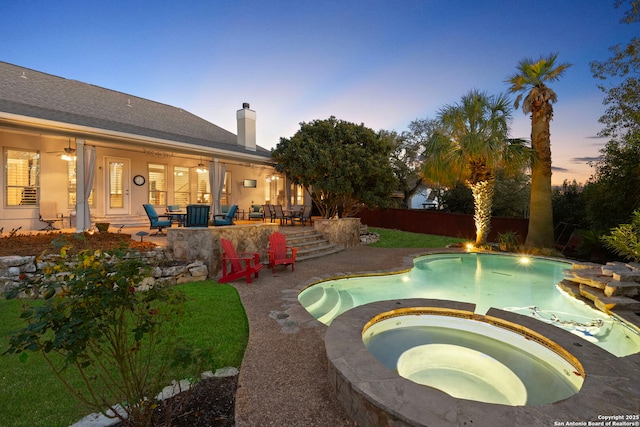 pool at dusk featuring a patio area and an in ground hot tub