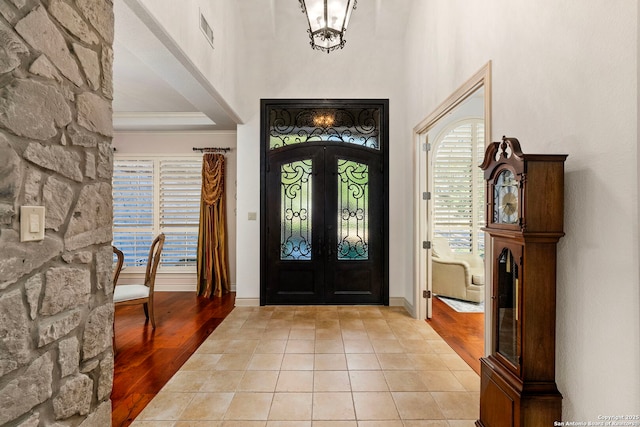 entrance foyer with crown molding, a chandelier, light wood-type flooring, and french doors