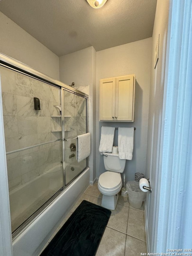 bathroom featuring tile patterned flooring, bath / shower combo with glass door, a textured ceiling, and toilet