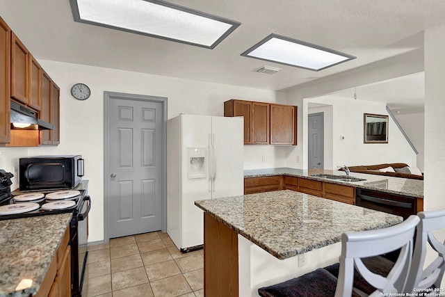 kitchen featuring sink, a kitchen bar, white refrigerator with ice dispenser, electric range, and light stone counters